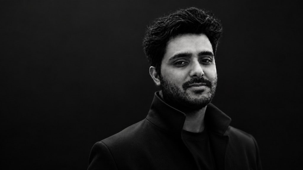 Black-and-white portrait of Dharminder Pal Singh in a dark coat against a dark background.